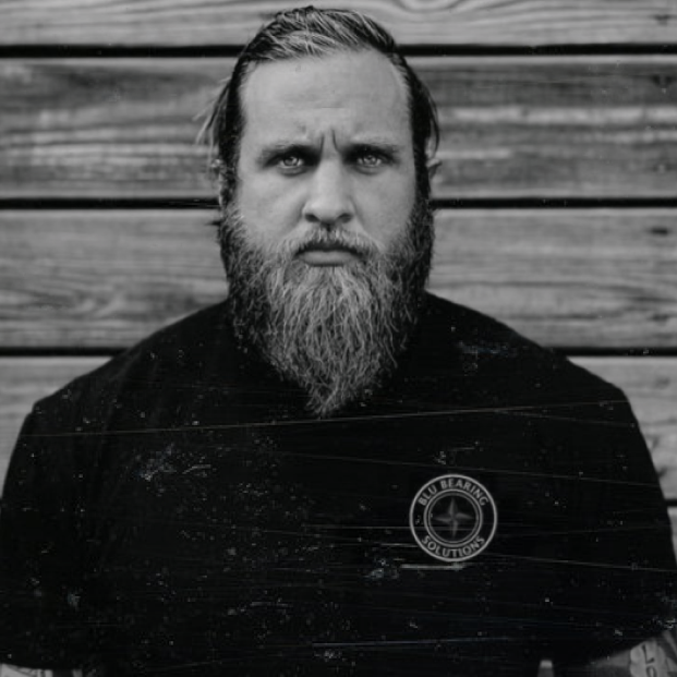 Black and white portrait of a bearded man against a wooden backdrop.