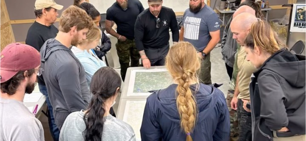 Group of people gathered around a table analyzing a map indoors.