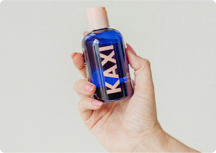 Hand holding a KAXI branded blue bottle with a pink cap.