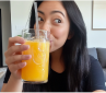 Person sipping orange juice from a glass with a straw.