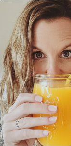 Person holding a glass of orange juice close to their face.