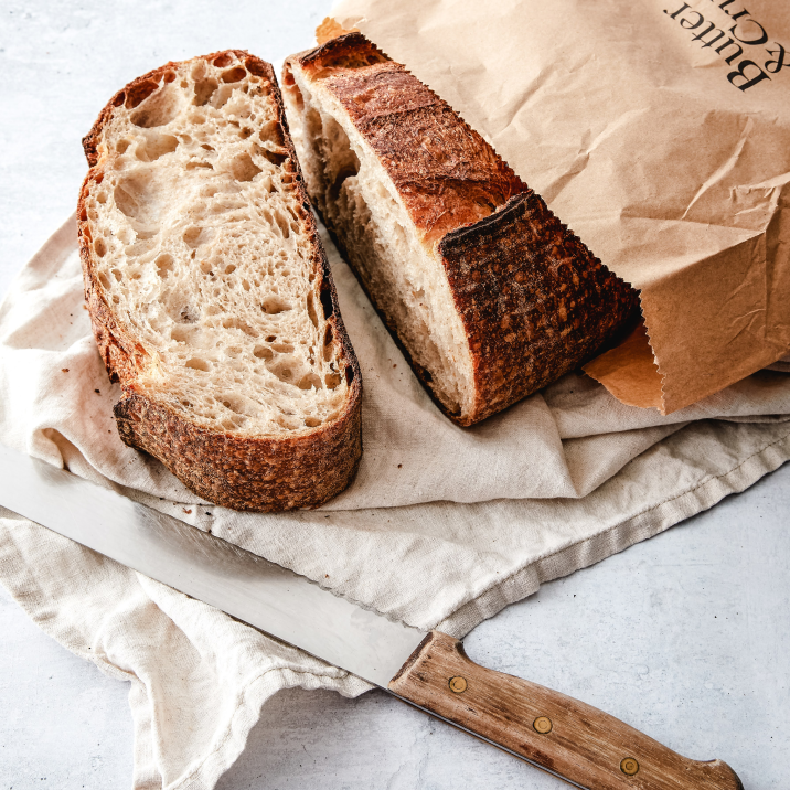 Sliced rustic bread on a cloth with a knife and paper bag.