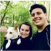 A couple smiles while holding a dog during a nature walk.