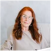 A person with long red hair sitting on a couch, wearing a beige top.
