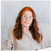 A woman with long red hair and glasses, seated and smiling.
