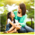 A mother and daughter sitting on grass, smiling at each other.