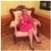 A person in a pink dress sitting on a cushioned chair in a warmly lit room.