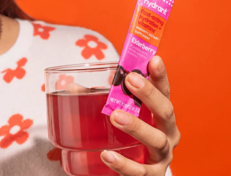 Person holding a glass of red drink and a packet labeled Elderberry.