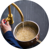 Person washing rice in a pot under running tap water.