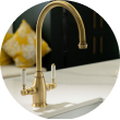 Elegant brass kitchen faucet over a white countertop with decorative pillows in the background.
