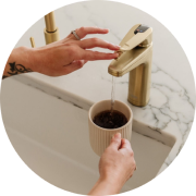 Hands filling a cup with water from a gold faucet.