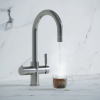 A kitchen faucet pouring water into a clear glass mug on a marble countertop.