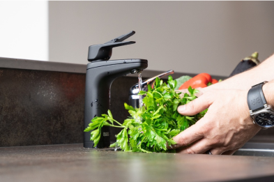 Person washing fresh herbs under a kitchen faucet.