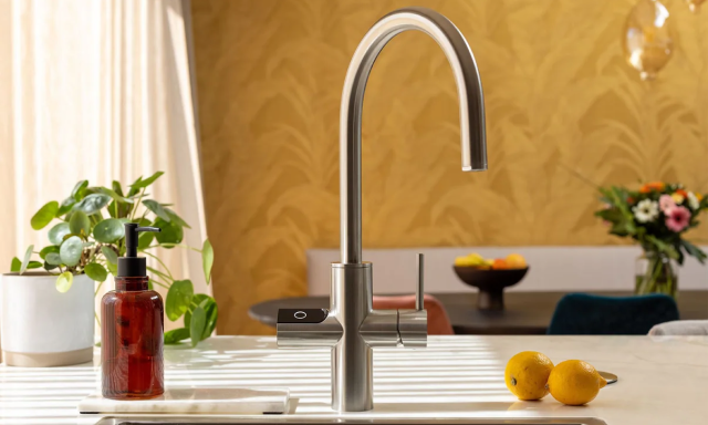 Modern kitchen faucet with a curved spout, next to lemons and a soap dispenser.