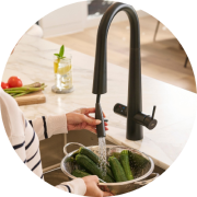 Person washing cucumbers in a kitchen sink with a black faucet.