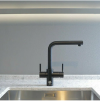 A modern black kitchen faucet over a stainless steel sink against a gray wall.