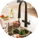 Person rinsing cucumbers under a modern black kitchen faucet.