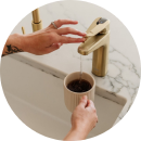 A person filling a mug with water from a modern gold faucet.