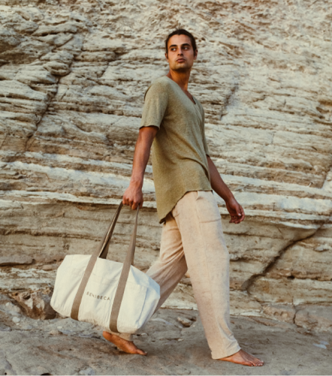 Man walking on rocky terrain with a beige bag.