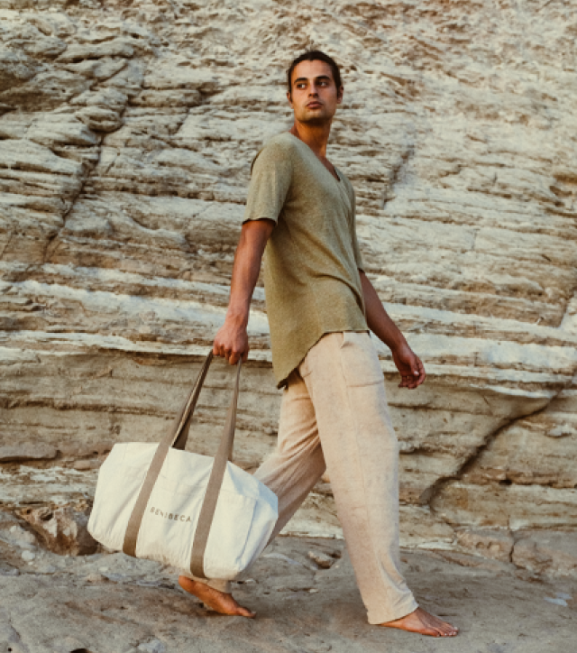 Man walking barefoot on rocky terrain, carrying a large white bag.