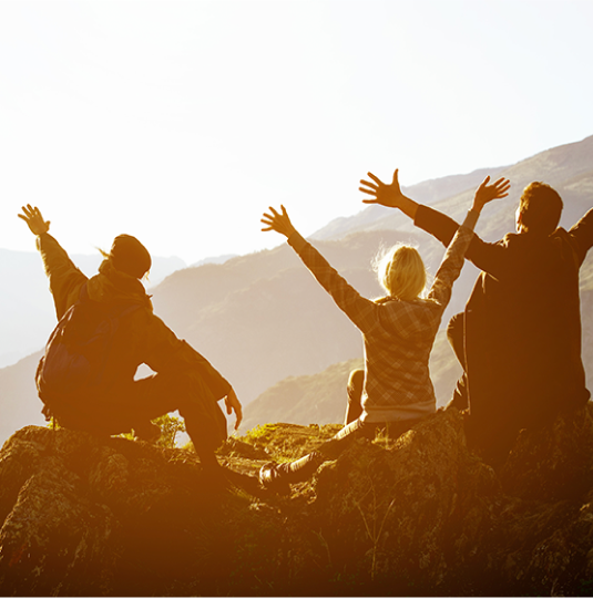 Three people sitting on a mountain, arms raised, enjoying the view.