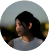 A woman with dark hair looking to the side, outdoors at sunset.