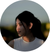Woman with long dark hair in a white top, looking to the side outdoors.
