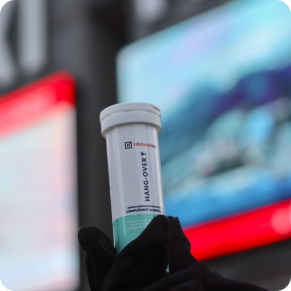 Eine kahle Hand hält eine Flasche mit der Aufschrift 'Hangover' mit blurred billboards im Hintergrund.