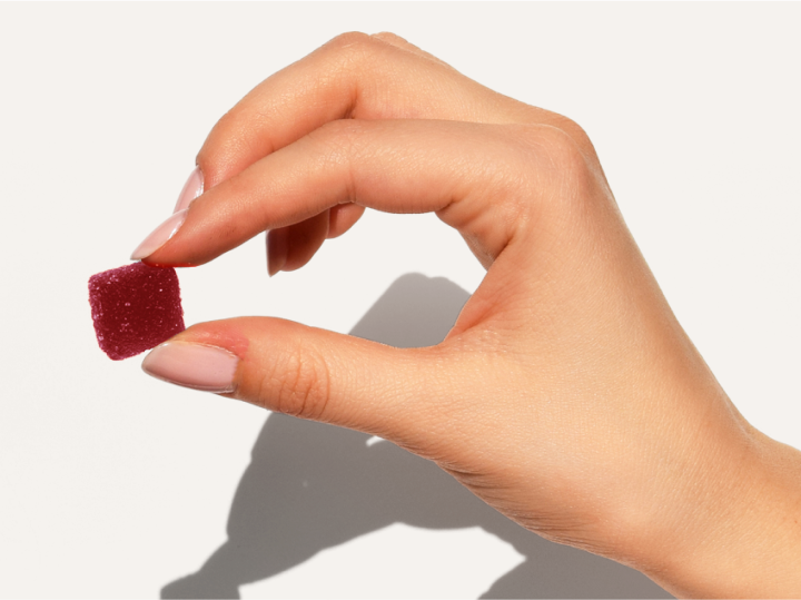 Hand holding a small red gummy candy against a plain background.