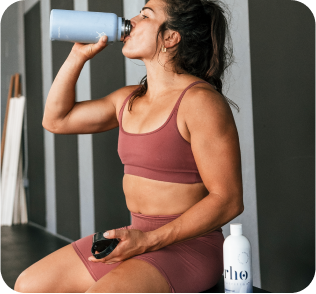 Athlete in workout attire drinking from a bottle, sitting on a bench.