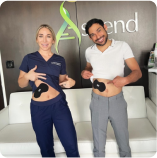 Two people display abdominal electrode devices, smiling, inside what appears to be a medical or wellness facility.