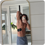 Man taking a mirror selfie while showing his toned physique and muscle stimulator device.