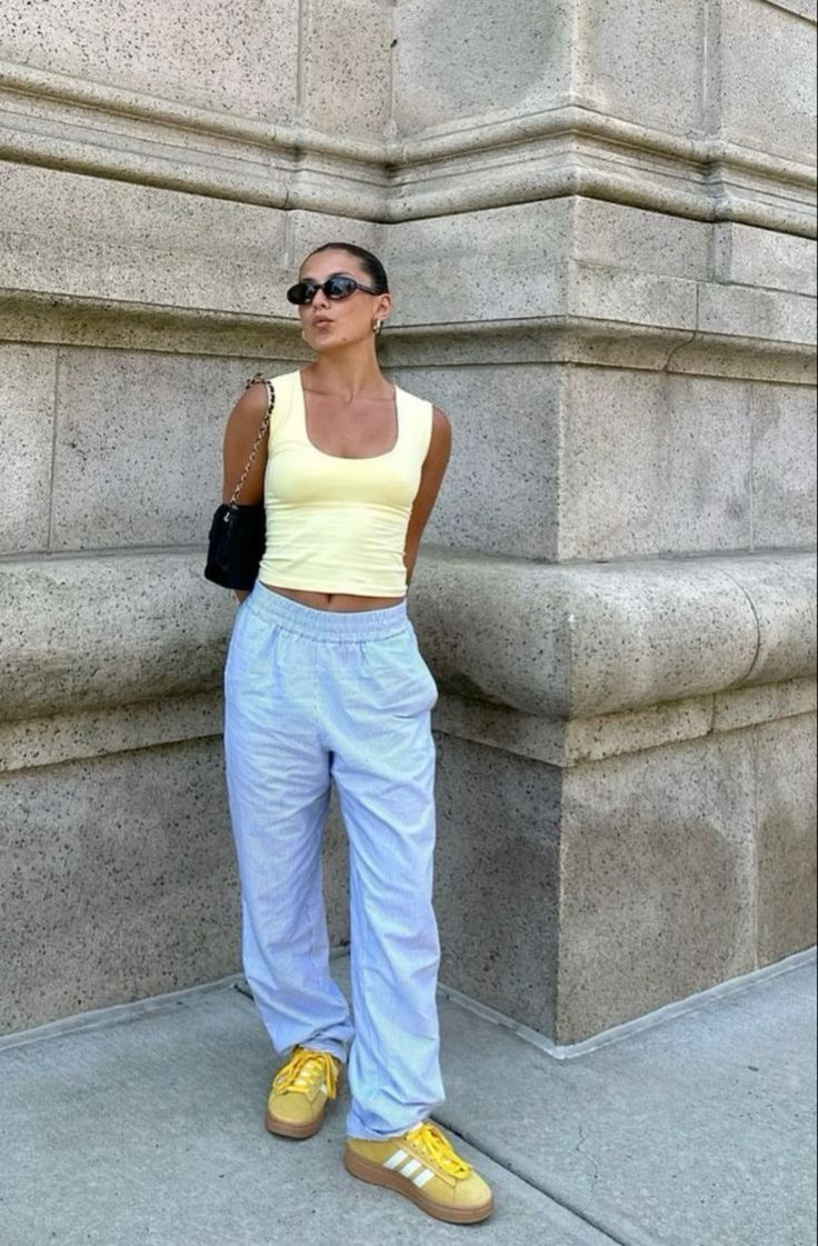 Person in yellow top and blue pants standing against a stone wall.