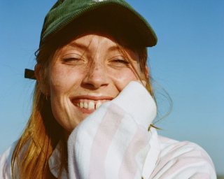 Person smiling under blue sky wearing a green cap and striped shirt.