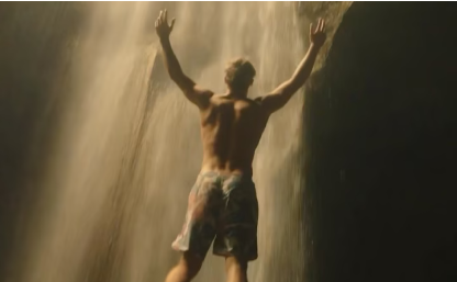 Person standing under a waterfall with arms raised.