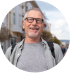 Smiling man wearing glasses and a backpack stands on a city street.