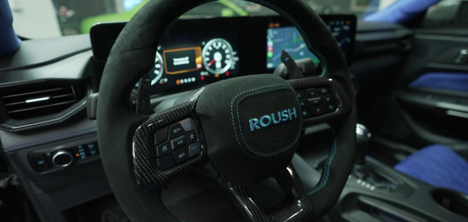 Steering wheel and dashboard of a car with 'ROUSH' logo.