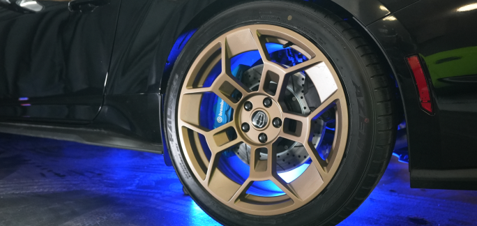 Close-up of a car wheel with bronze rims and blue underglow lighting.