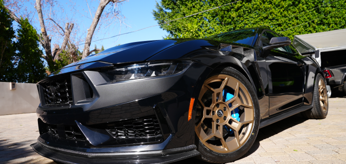 Sleek black sports car with bronze wheels parked on a sunny driveway.