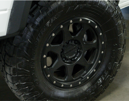 Close-up of a black, rugged off-road tire and wheel on a white vehicle.