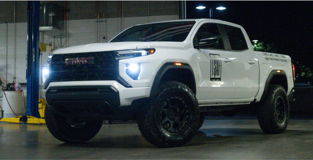 White pickup truck with bright headlights in a garage setting at night.