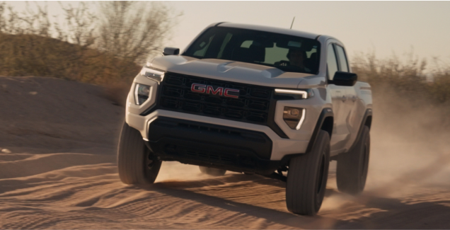 A GMC truck driving on a sandy terrain, kicking up dust.