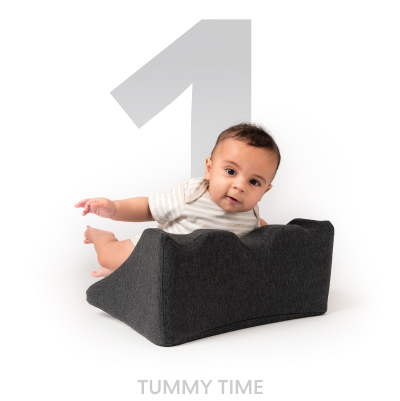 Baby on a gray wedge cushion for tummy time.