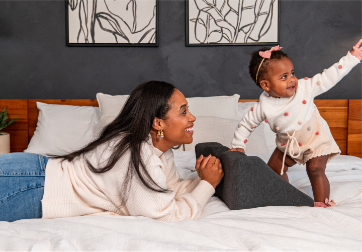 Mother and baby happily playing on a bed with decorative wall art behind them.