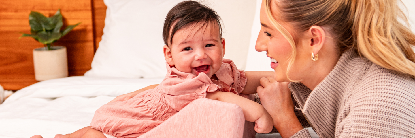 A mother and baby smiling and playing together on a bed.