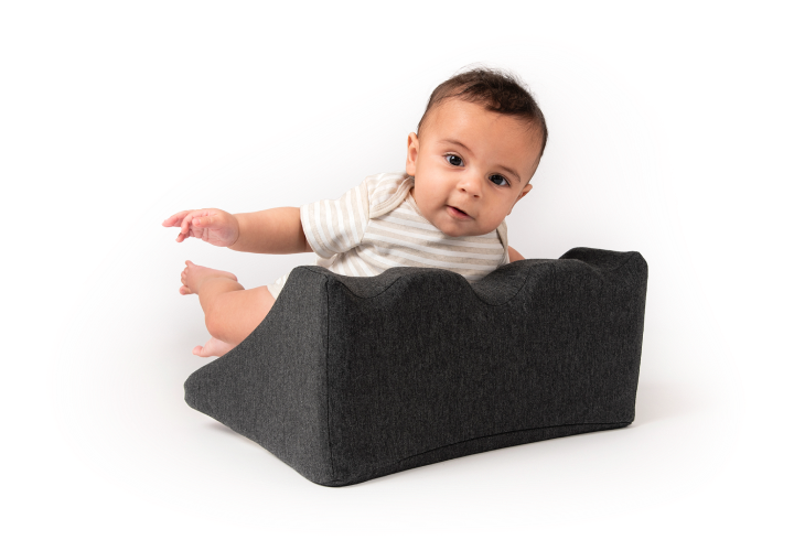Baby lying on a gray, curved cushion.