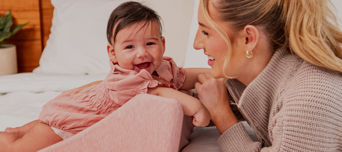 A baby and a woman smiling at each other while laying on a bed.