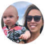 A woman wearing sunglasses holding a baby dressed in a tropical shirt.