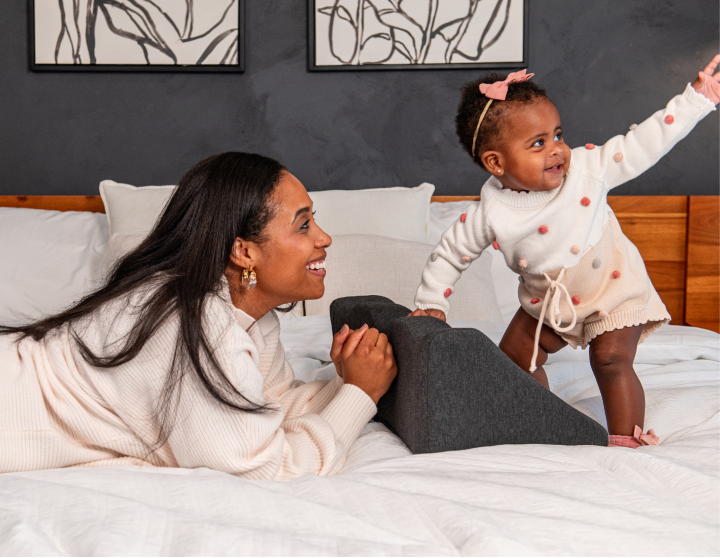 Woman and baby playing on a bed, smiling and interacting happily.