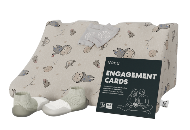 Set of baby items including engagement cards, socks, and shoes on a cushioned surface with a space theme.